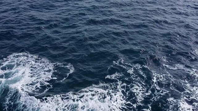 Deep blue ocean water moving with white foam and waves. A serene and powerful natural background view from a moving ship creating a wake
