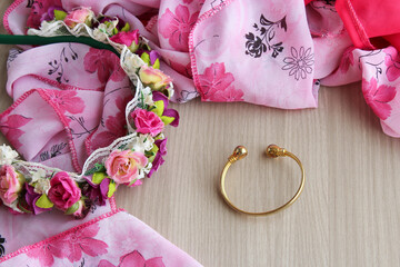 Golden bracelet and pink flower tiara on wooden background. Perfect for feminine fashion accessories, beauty branding, costume jewelry themes, and lifestyle content.