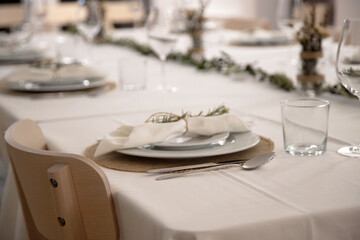 Fototapeta premium A neatly arranged dining table shows a single place setting with white plates, cutlery and a cloth napkin tied with twine and fresh rosemary, prepared for an elegant family dinner in a cozy home.