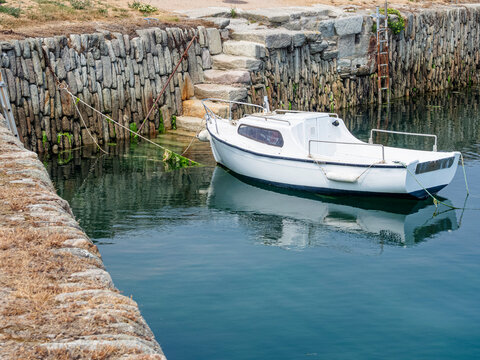 Barco blanco amarrado en las aguas del Puerto de Becquet , con reflejos y escaleras de acceso, viajando por la Normand&iacute;a Francesa en verano de 2022