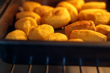 Golden roast potatoes bake in a hot oven tray in a home kitchen, their crisping edges and warm...