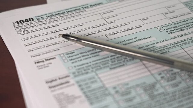 A taxpayer completes the 1040 Individual Income Tax Return form on a table. The form contains sections detailing personal information and income for the tax year 2025