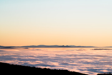 Fototapeta premium Pink sea of ​​clouds at dawn, silhouette of mountains, soft pastel sky, peaceful winter landscape, inspiring panorama, dreamy atmosphere, travel concept.