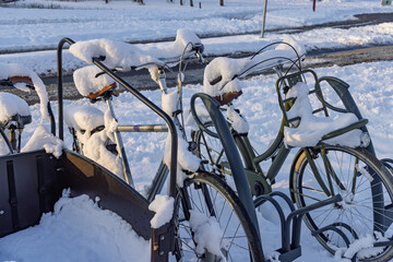 Close-up of Dutch bicycles and a cargo bike covered in snow parked at a bike rack during a cold winter day in the Netherlands.