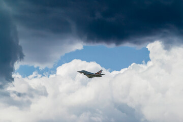 Fototapeta premium Military fighter jet flying through the sky during an aerial demonstration, framed by clouds and open blue space