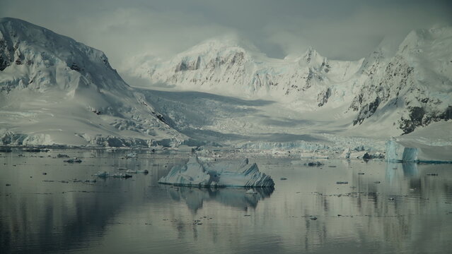 White Iceberg in Antarctica with snow mountains reflection in foreground.Misty snowy backdrop - Powered by Adobe