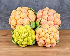 Three colorful cauliflower heads with green leaves on a wooden table against a gray background