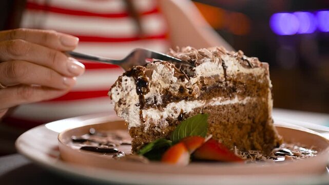 A close-up of a fork taking a piece from a rich spongy chocolate cake on a plate