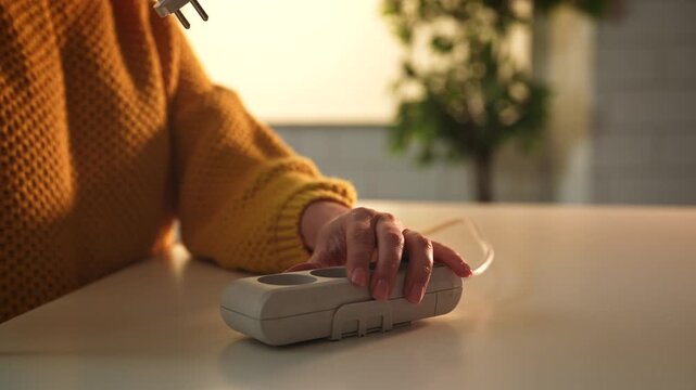 Close up of hands inserting a power plug into a surge protector on a table, with a blurred background.