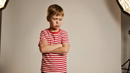 Angry little boy with arms crossed pouting in a studio. Upset and stubborn child with a grumpy expression on a white background. Childhood emotions and behavior
