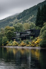 Fototapeta premium A contemporary house nestled by the serene lake, enveloped by a lush forest and majestic mountains, all beneath a blanket of overcast skies