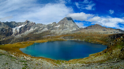 Matterhorn reflected in an alpine lake with clear water, rocky shoreline, and surrounding high altitude terrain in Switzerland. Mountain landscape showing iconic peak, glacial environment, natural sym