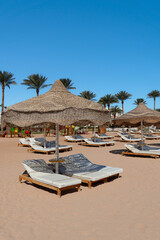Vertical shot of white sun loungers and woven straw umbrellas on a clean, sunny sandy beach at a tropical resort