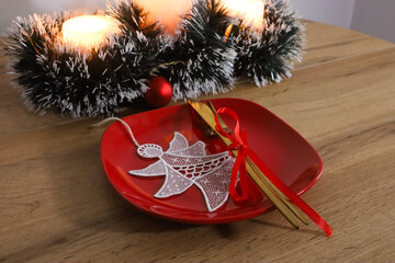Red plate with gold cutlery tied with red ribbon lace angel ornament and Christmas candle...
