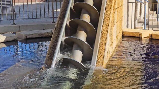 Close-up horizontal view of an Archimedes screw rotating and lifting water. Engineering mechanism used for water management, drainage systems, and hydraulic infrastructure.