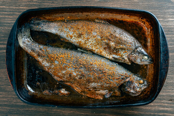 Delicious baked two trout fish with spices in a glass baking dish, closeup, top view