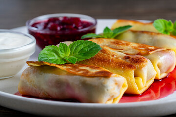Fried rolled pancakes stuffed with cottage cheese and cherry, sweet dessert on plate, closeup. Homemade baking. Delicious fast food for breakfast. Wrapped pancakes with sour cream and jam