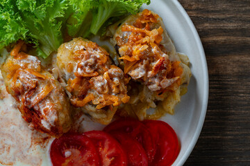 Three delicious cabbage rolls stuffed with meat and rice on a plate along with sour cream and lettuce, closeup, top view