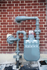 Gas meter and utility pipes installed on brick wall of residential building
