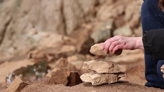 A woman stacks stones one on top of the other, making a wish. Stacking stones into a tower in a cave. Prohodna Cave, popular names &mdash; Eyes of God or Devil&rsquo;s Eyes. Bulgaria
