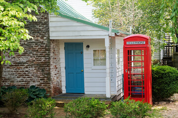 Vintage British style red phone booth in quiet residential garden next to white house exterior