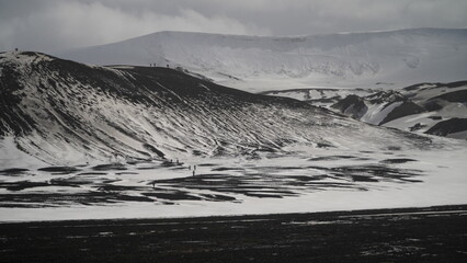 Antarctica , Volcanic rock mountains lighty covered in snow , black ice , snow mountain in background ,with cloudy stormy weather and antsize explorers