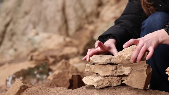A woman stacks stones one on top of the other, making a wish. Stacking stones into a tower in a cave. Prohodna Cave, popular names &mdash; Eyes of God or Devil&rsquo;s Eyes. Bulgaria