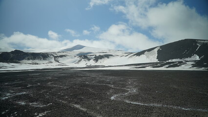 Black Lawa foreground with snow covered lawa mountains and snow mountain in backgroung , blue sky with white clouds Antarctica © Amelia