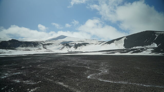 Black Lawa foreground with snow covered lawa mountains and snow mountain in backgroung , blue sky with white clouds Antarctica