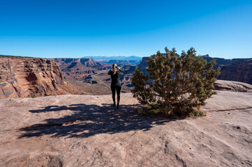 Woman photographs Shafer Canyon from Shafer Trail in Canyonlands National Park, Utah on clear sunny winter day.