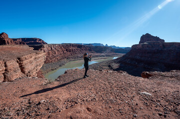 Fototapeta premium Woman photographs Colorado River from overlook on Potash Road near Moab, Utah on clear sunny winter day.