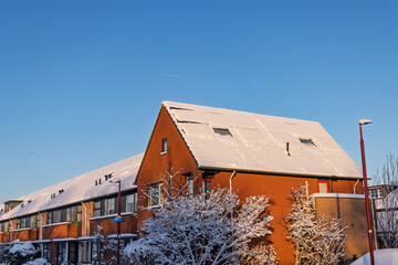 Row of brick residential houses in the Netherlands with solar panels covered in snow under a clear blue sky, showing winter energy challenges.