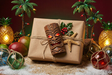 A festive tropical Christmas concept. A gift decorated with a Tiki mask and holly, surrounded by sand, pineapples, and palm tree lights.