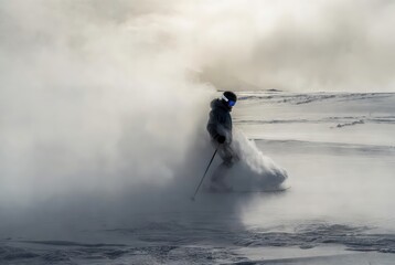 Skier carving deep powder snow creating dramatic spray while descending steep mountain slope during winter storm with foggy blurred background, concept of adrenaline fueled freeride and extreme winter