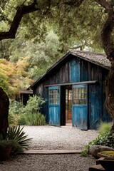 Old blue wooden building stands among trees and plants in a garden during daylight with a gravel path leading to open doors