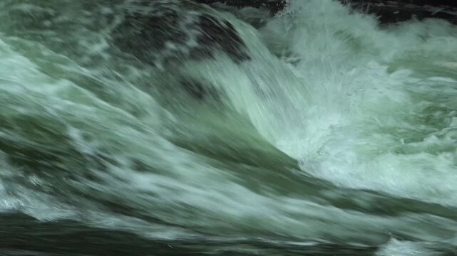 A close-up of rapids flowing over a rock, creating a hole in a raging river.