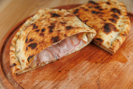 Explore delicious calzone with ham and cheese on wooden board served in a cozy kitchen area during dinner time