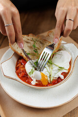 Enjoying a delicious poached egg dish with fresh bread and vegetables on a wooden table