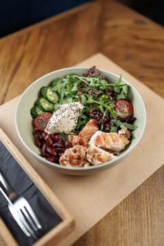 Fresh salad bowl with grilled chicken, beans, vegetables, and yogurt served in a cozy restaurant setting