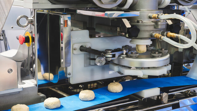 A conveyor belt with four doughnuts on it, being made by a machine. Bread production concept background.