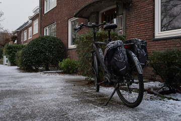 Obraz premium An unexpected snowfall lightly blankets a parked bicycle against the backdrop of a cozy Dutch home, symbolizing a quiet pause in daily routine.