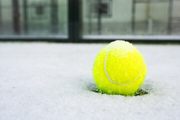 A lone padel ball rests in fresh snow on an outdoor court, highlighting the sport's seasonal...