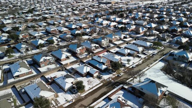Frisco, Texas, USA - January 3rd, 2024: Drone view of extensive suburban neighborhood with hundreds of single-family homes, snow on roofs, streets and yards under sunny winter conditions