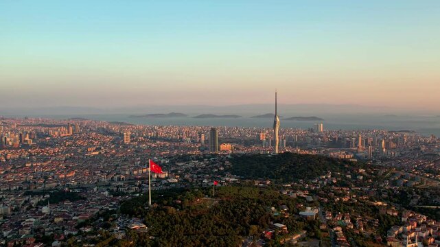 Drone footage showing Camlica Hill with its large Turkish flag, Camlica Tower and the vast Istanbul skyline illuminated by warm sunset colors over the Marmara Sea.