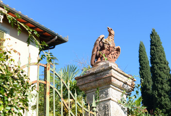 Obraz premium Ancient sculpture of an eagle on stone socket at iron gate with clear blue sky on an october day in Poggibonsi, Tuscany