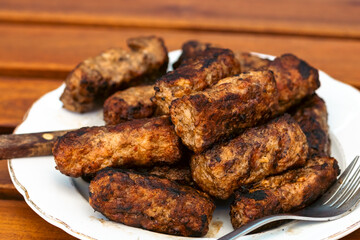 Preparing traditional Romanian meat rolls called mici or mititei on a hot barbecue grill with fire flames