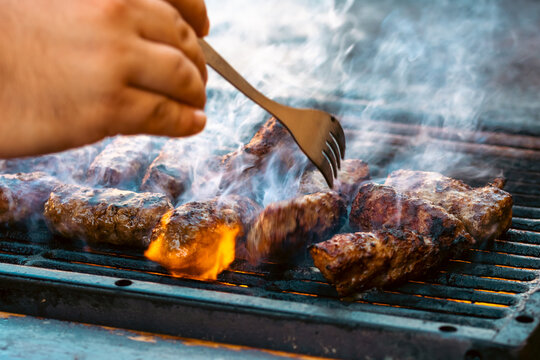 Preparing traditional Romanian meat rolls called mici or mititei on a hot barbecue grill with fire flames