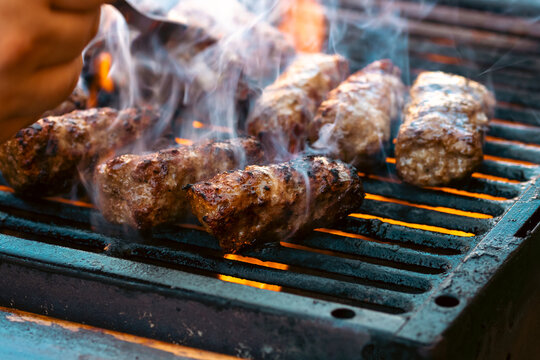 Preparing traditional Romanian meat rolls called mici or mititei on a hot barbecue grill with fire flames