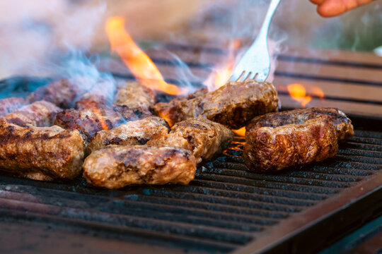Preparing traditional Romanian meat rolls called mici or mititei on a hot barbecue grill with fire flames