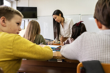 The students are taking an exam in the classroom, focused on their papers. The teacher walks around the room, quietly checking on their progress.	
